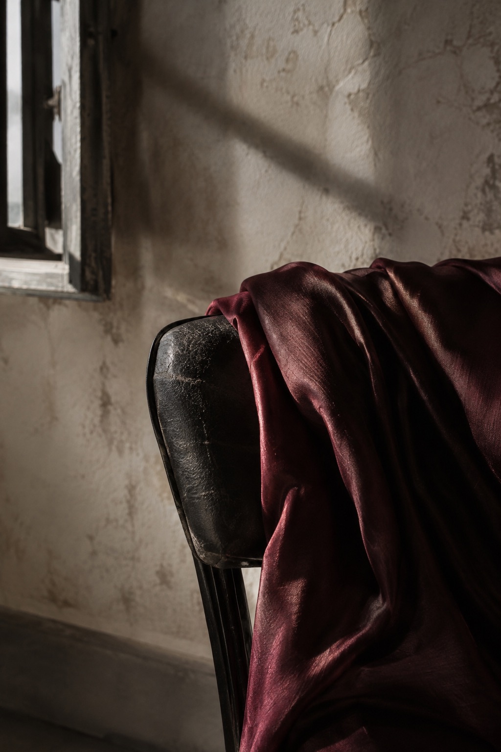 Burgundy silk resting on a black leather chair beside a sunlit window